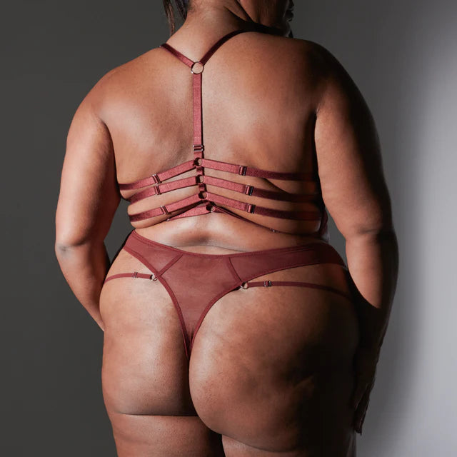 size 2x black model shows off the strappy back of the bralette and thong from thistle & spire